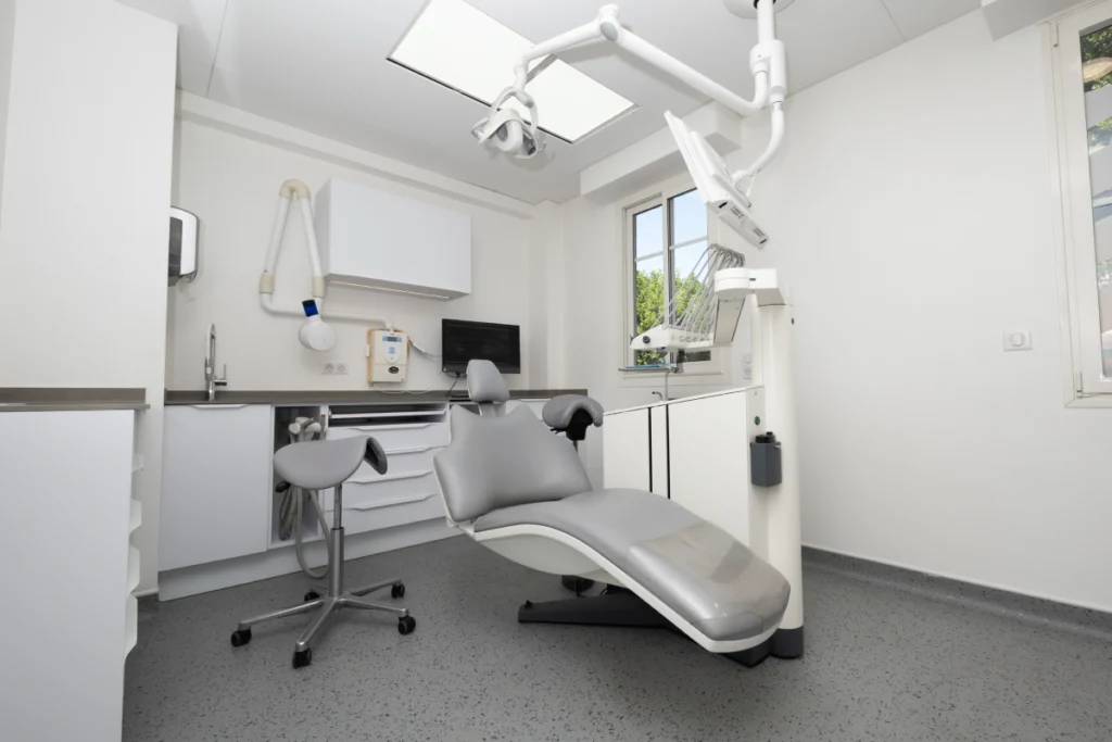 Salle de soins vide avec fauteuil gris et lampe suspendue